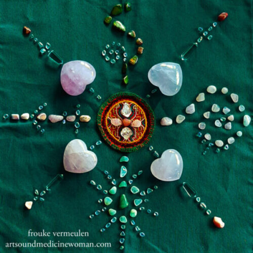 Heart aches and altars - altar. Composition of gemstones on green altar cloth. In the middle lays a circular 7cm-diameter Shipibo cloth with green, yellow, red and white threads. Around it four rose quartz hearts are positioned with their tips pointing outwards. At their tips a clear quartz dubble pointer is positioned, together with tiny Angel Aura chips. In between each pair of hearts gemstones are forming different shapes: spirals, sun-like structures, curves and straight lines.